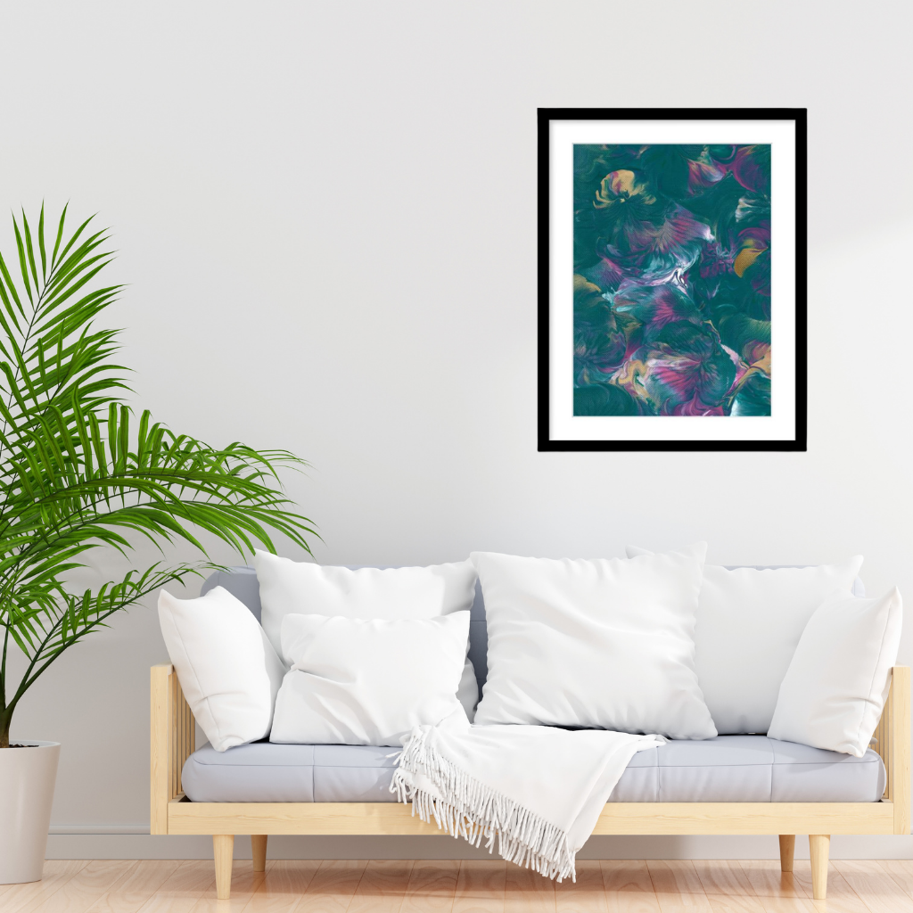 An A1 framed abstract art print featuring colourful teal, green, pink, and gold tones, displayed above a modern light wood sofa with white pillows and a white throw blanket.
